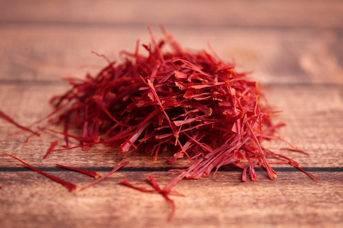 Saffron threads are gathered in a small heap on a wood table